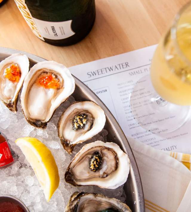 Sweetwater Oyster Bar plate of caviar topped oysters next to white wine on a menu