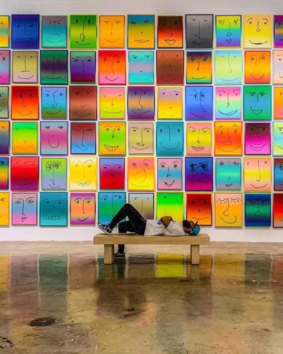 A man laying on a bench in front of the Happy Exhibit at NSU Art Museum