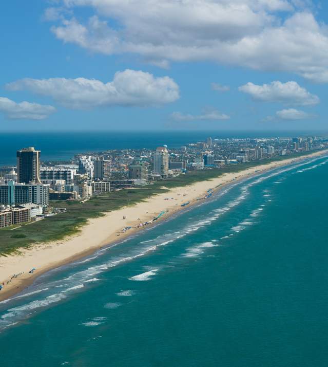 Aerial view of South Padre Island showing a long sandy beach, turquoise Gulf waves and high-rise hotels along the shoreline
