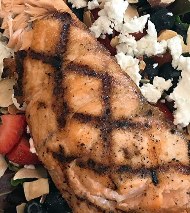 Grilled salmon fillet on a colorful salad with mixed greens, strawberries, almonds, feta, and croutons.