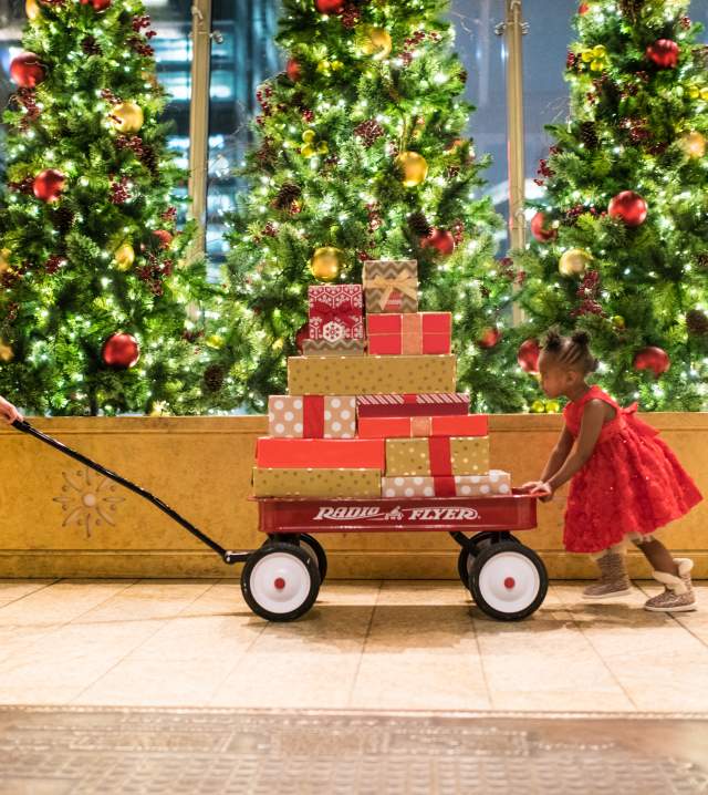 A mom pulling a radio flyer wagon loaded with presents and a child pushing it from behind