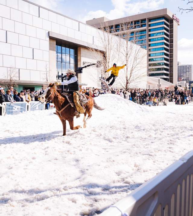 In this photo, a man is riding a horse dragging a skier off a mound on West Temple in Downtown Salt Lake. The road is covered in snow and the photo is from a 2024 event in February called Winter Roundup.