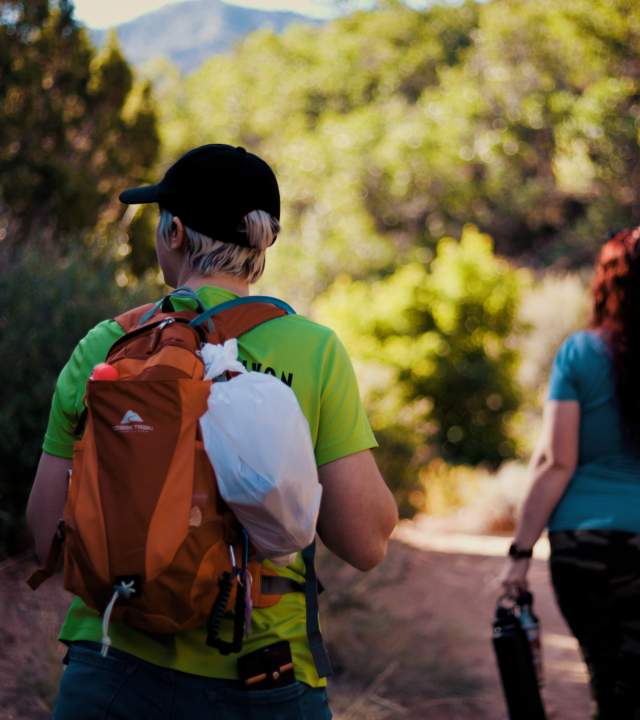 Family hiking through a red rock canyon on the Spring Creek Trail in Kanarraville Utah. A woman in the foreground has a small white trash bag attached to her bag for picking up litter.