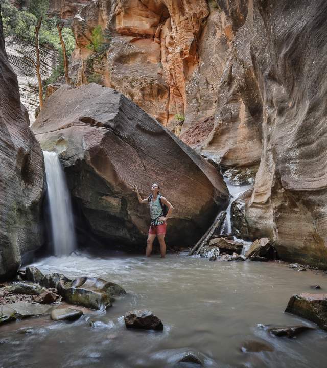Woman standing beside a waterfall within a red rock slot canyon in southern Utah.