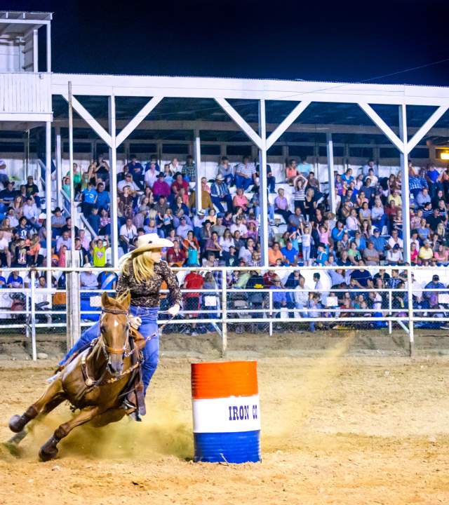 A barrel racer rounds a red, white, and blue barrel in front of a full stadium at the Iron County Fair in Parowan, Utah.