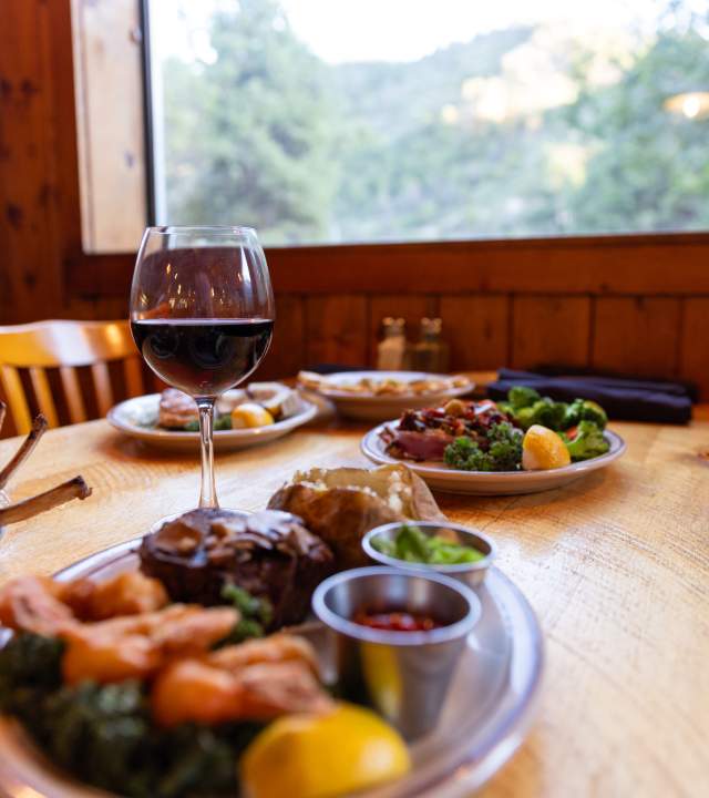 A table laid out with steaks, steamed vegetables, and a glass of red wine at Milts Stage Stop in Cedar City.