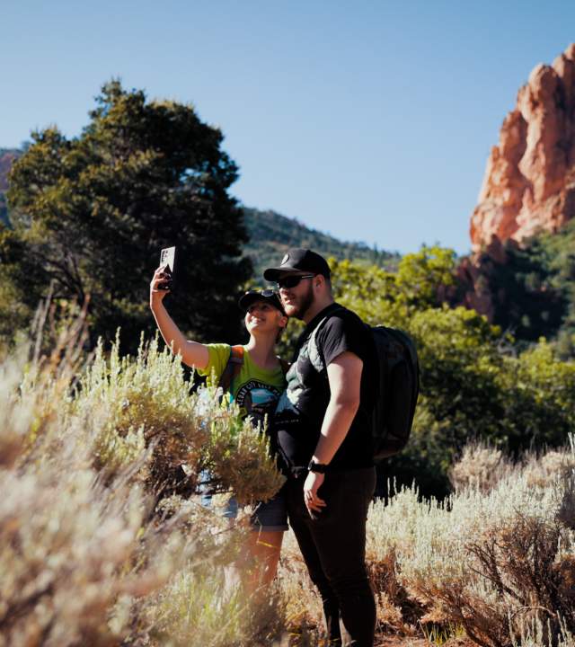Couple taking a selfie on the Spring Creek Trail in Kanarraville, Utah with red rock formations in the background, surrounded by pale sagebrush.