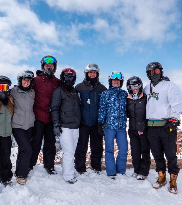 A group of eight adults dressed for winter recreation stand together for a photo at the North Overlook of Cedar Breaks National Monument