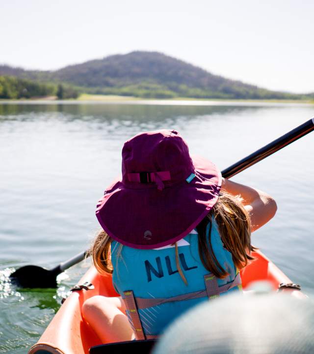 Person in a purple hat and bright blue life preserver kayaks on Navajo Lake in Southern Utah