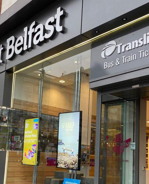 An exterior of the Belfast Welcome Centre with a tourist using a touch screen inside.
