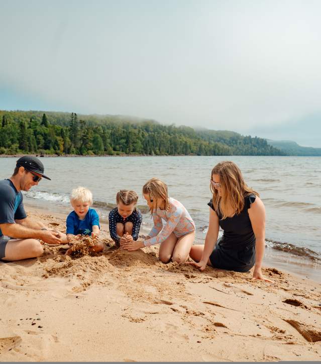 parents and three children lay in the sand, playing and laughing along the lake's edge