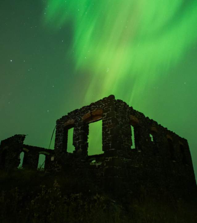 northern lights paint the sky with a ruin in dark silhouette in the foreground