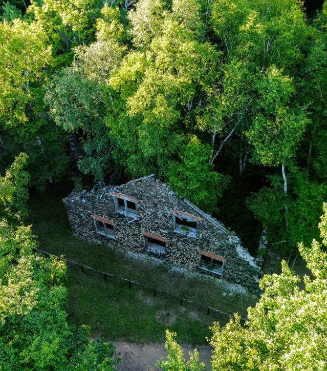 a top down aerial view of thick forests with the ruins of a stone mining era outbuilding