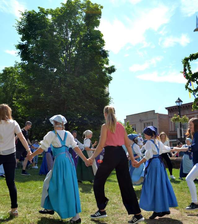 a large group in traditional finnish attire pose with finnish and american flags