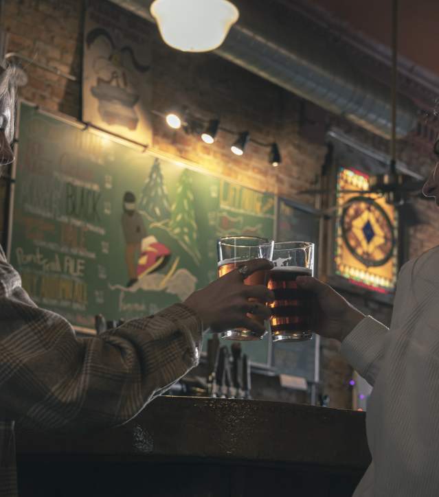 two people cheers pints of beer inside the keweenaw brewing company tap room