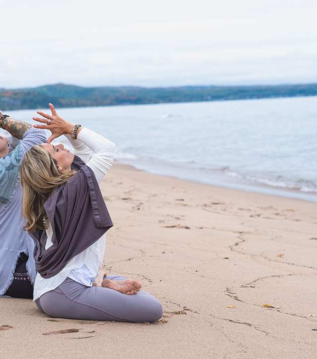 2 women practice yoga on the sandy beach.