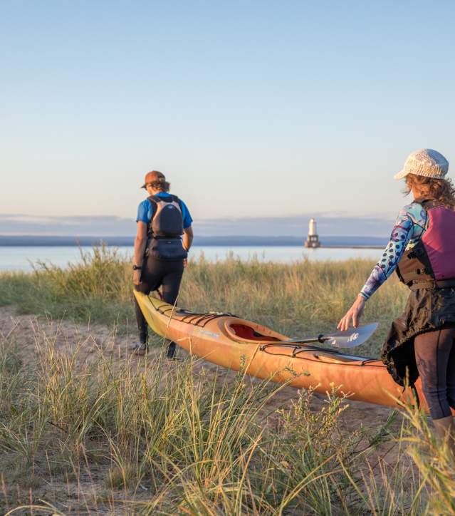 2 people carry a kayak to the shoreline.