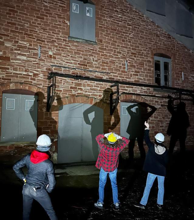 people in hardhats play with shadows against a brick building