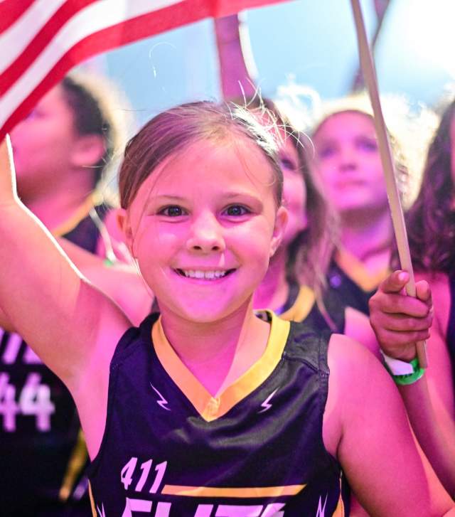 A young girl in sports clothes smiles while holding an American Flag.