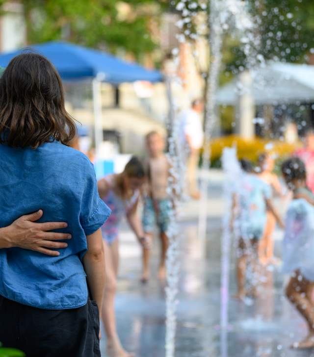couple embracing as they watch kids splash in a fountain