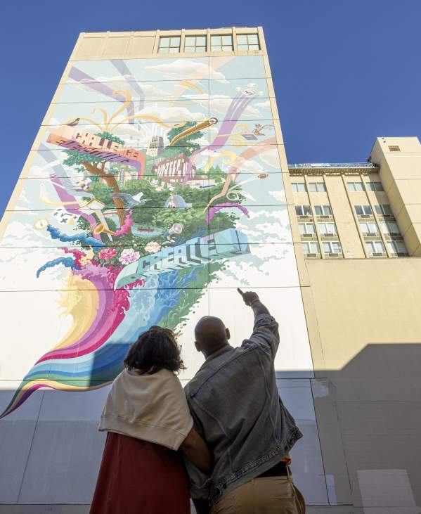 Couple pointing upward at tall, colorful mural
