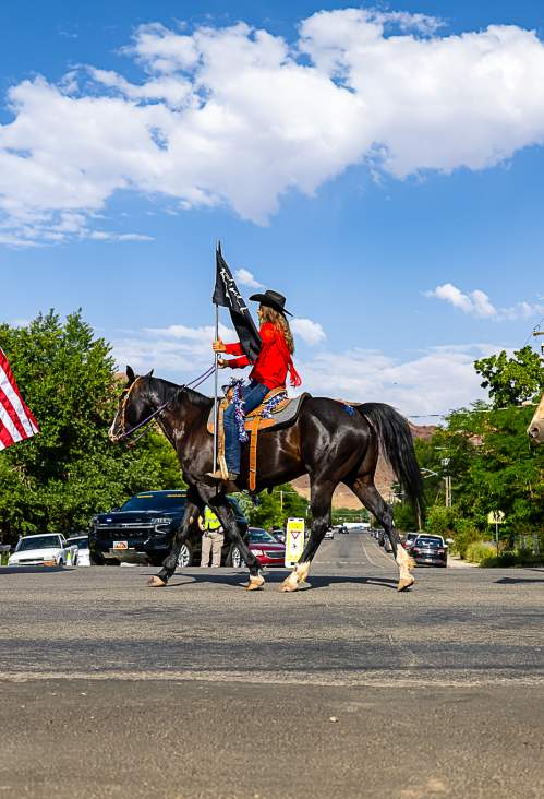 Three women riding horses and holding flags in the Moab 4th of July parade.