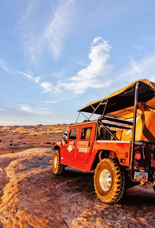 A red off-roading Hummer crawls over Moab’s iconic red rock at sunset.
