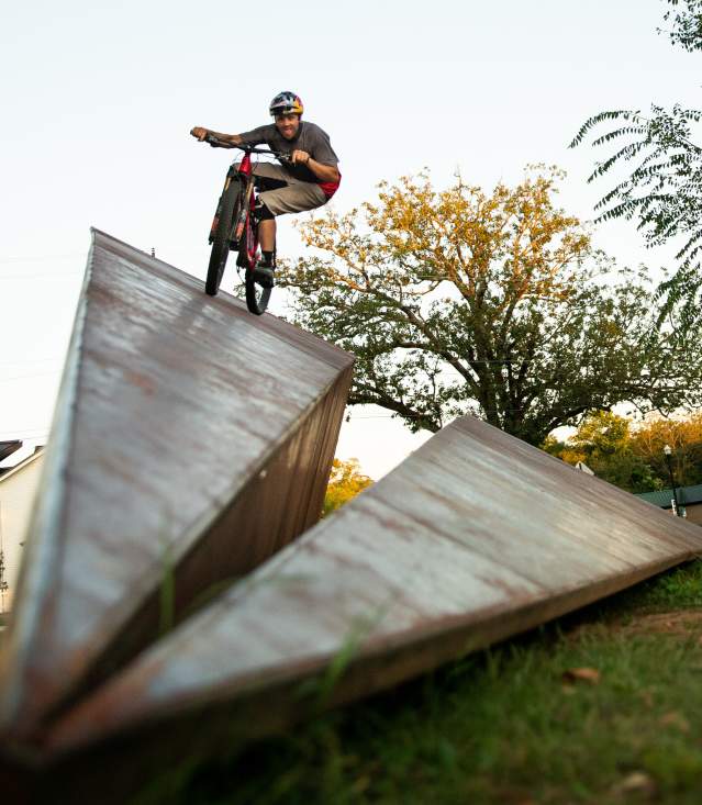 A larger than life sculpture of a paper airplane with a mountain biker doing tricks on it.