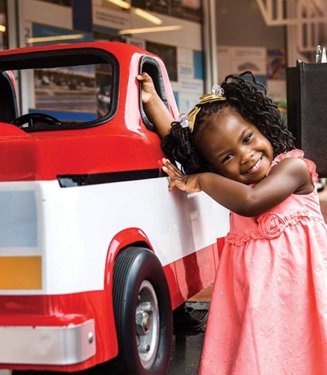 Image of a happy young girl leaning against a a coin operated replica of Sam Walton's truck