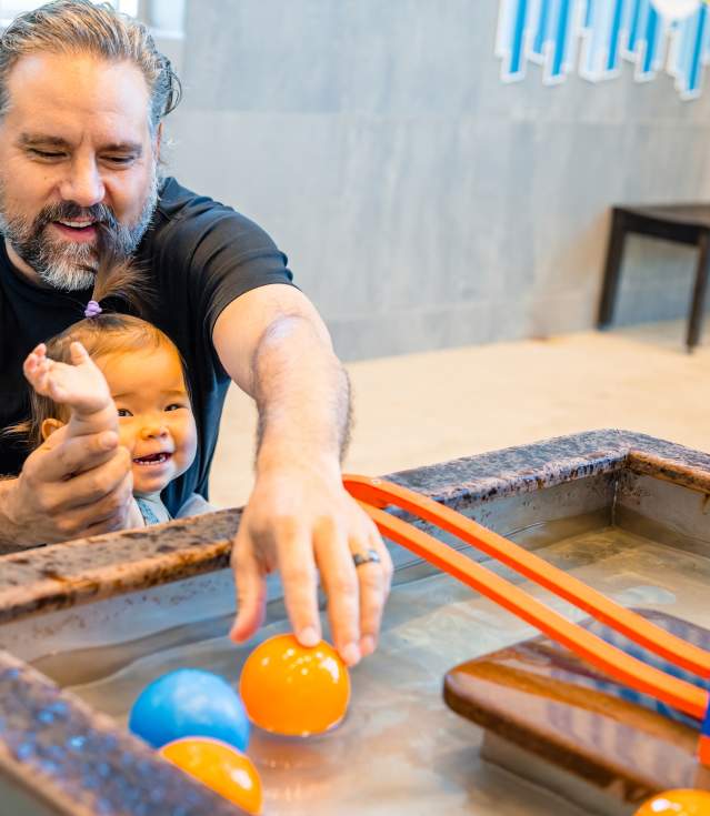 Father and young baby playing with ball in water feature at the Amazuem.