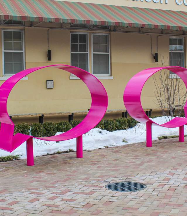 Two large pink speech bubble sculptures are displayed in front of a beige building with "Benton County Circuit Court Division II" signage. Snow covers the ground, and greenery is visible nearby.