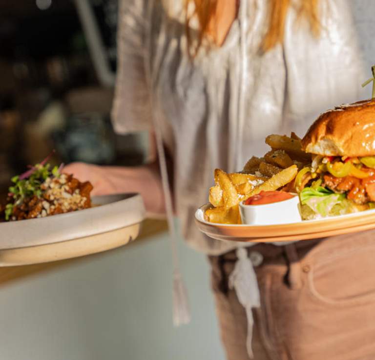 Woman carrying two plates of food - one with a hamburger, the other obscured in the distance