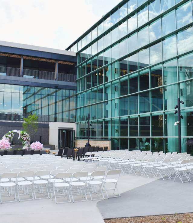Outdoor wedding set up with white chairs, pink flower arrangement at the front with towering Central Park windows surrounding the scene.