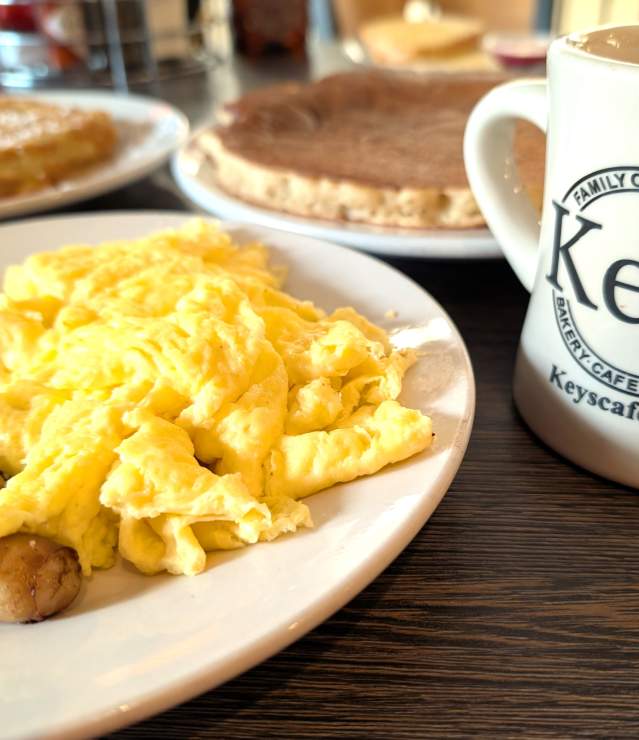 Breakfast items--eggs, sausage, pancakes and French toast--with a coffee featuring Key's Cafe logo on cup.