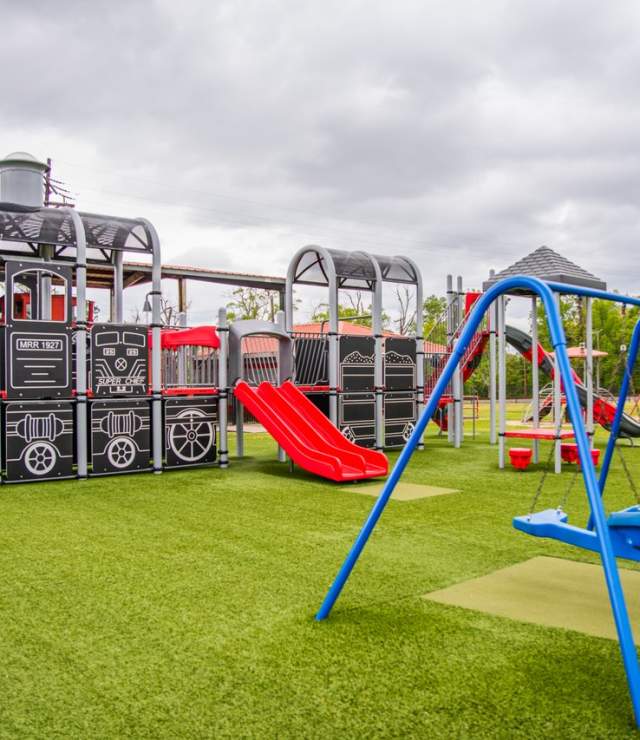 railroad themed playground with a model train, slide, and swing set