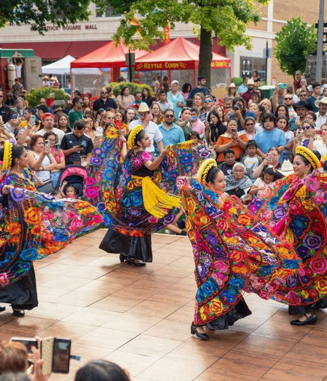 Woman dancing in colorful garments on a stage in a crowd.