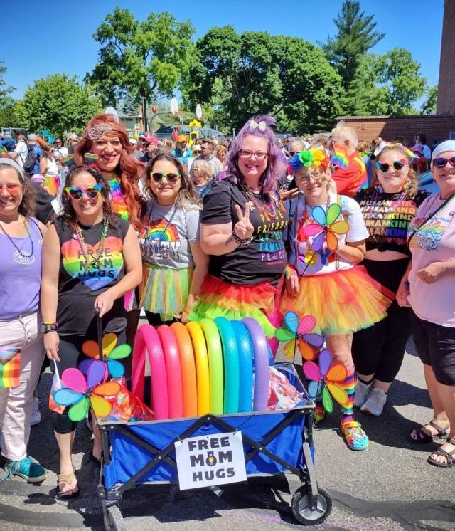 Group of people in colorful outfits with a rainbow wagon at the parade