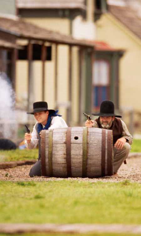 Two men hide behind a barrel in a reenactment at Boot Hill Museum