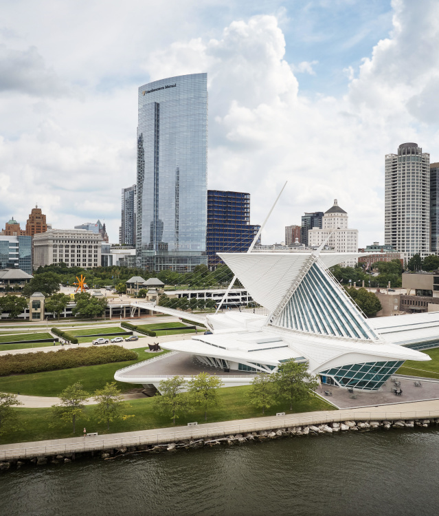 Milwaukee skyline featuring the Milwaukee Art Museum’s iconic white Quadracci Pavilion with its wing-like Burke Brise Soleil along Lake Michigan, surrounded by downtown high-rise buildings including the US Bank Center and Northwestern Mutual Tower under a partly cloudy sky.