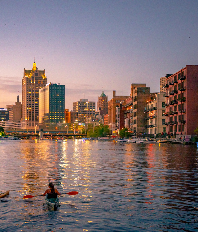 two kayakers on the Milwaukee River overlooking Milwaukee's Historic Third Ward and the skyline