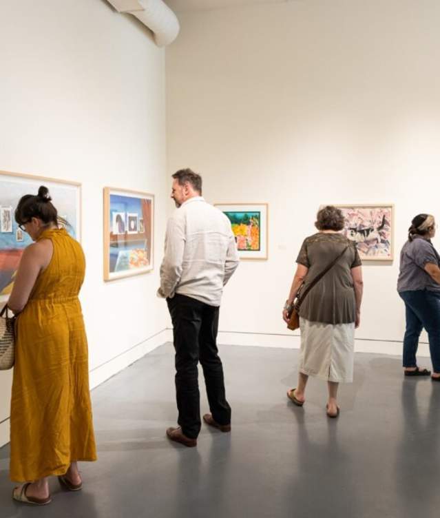 A group of people viewing art hung on a wall during 2nd Friday Norman Art Walk
