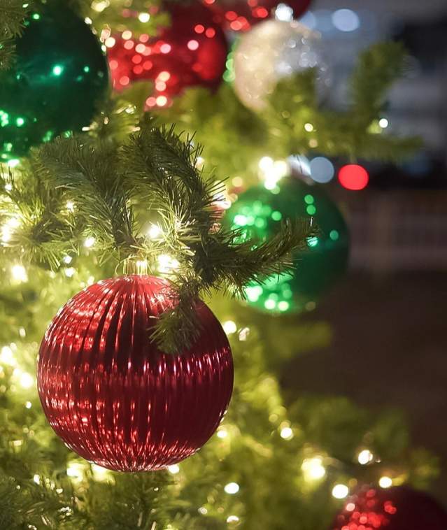 a close-up photo of red and green Christmas balls hanging on a lit Christmas Tree