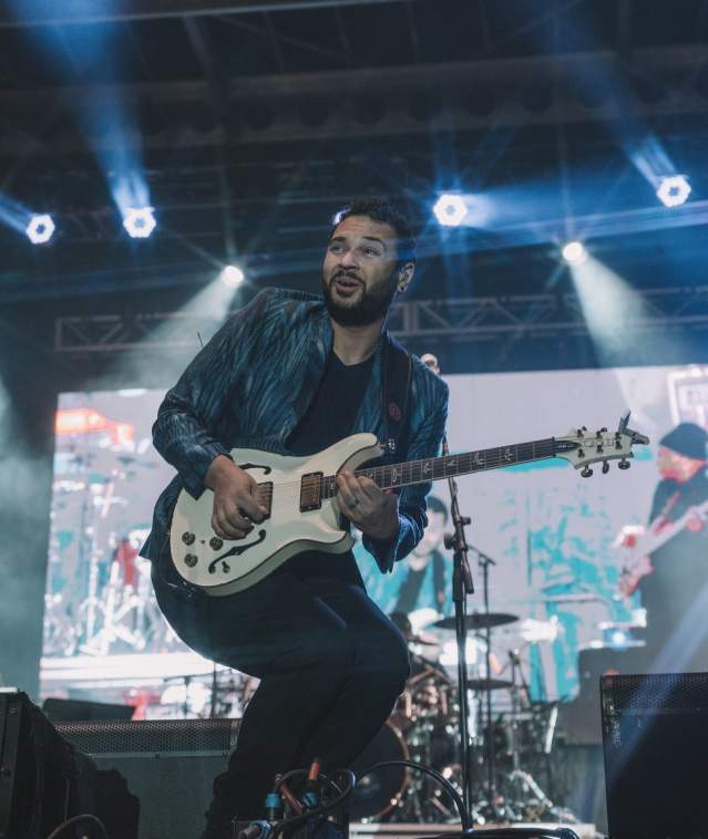 A performer on an outdoor stage at night, playing the electric guitar