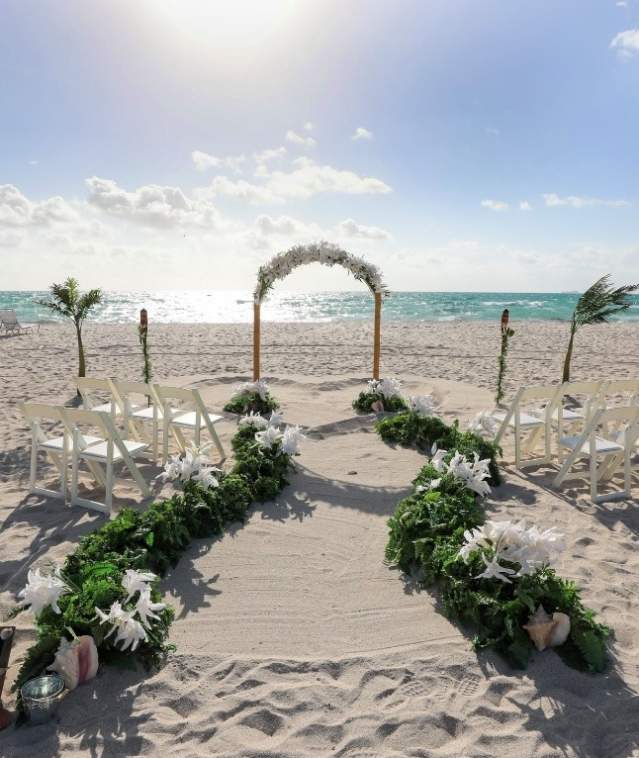 A wedding set-up on the beach with 10 chairs on either side of a flowered arch