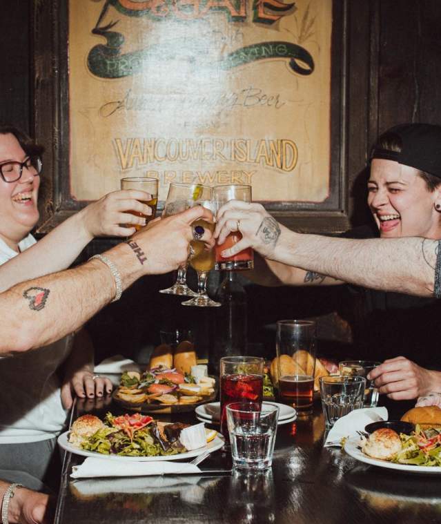 Four people at a restaurant table raising glasses in a toast over food.