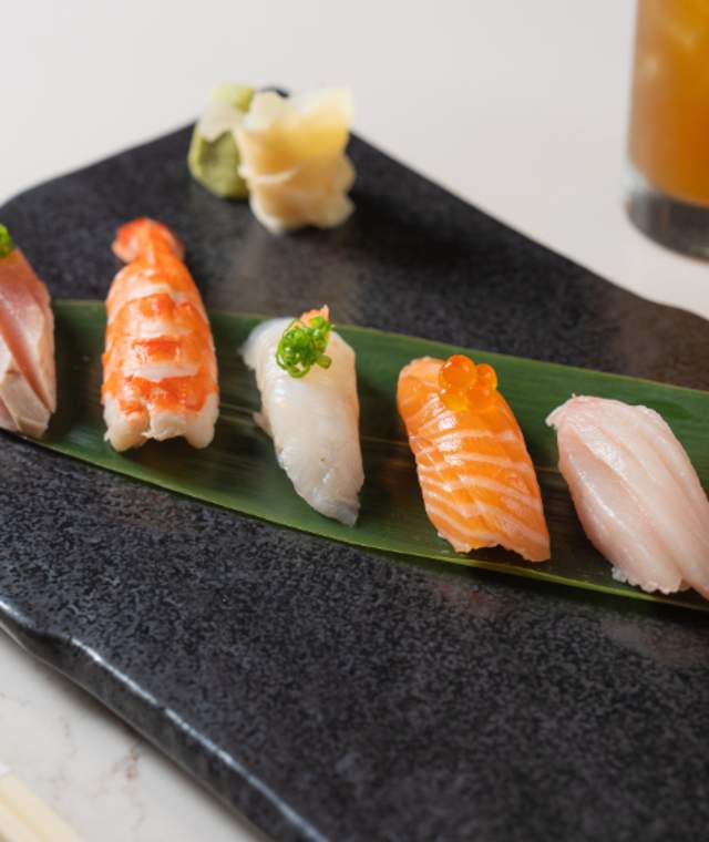 Five different nigiri sushi options beautifully plated on a black plate.