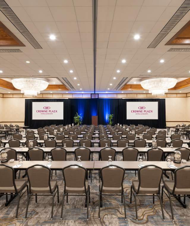 ballroom of the Crowne Plaza Phoenix Chandler Golf Resort set with tables, chairs and screens with overhead chandeliers