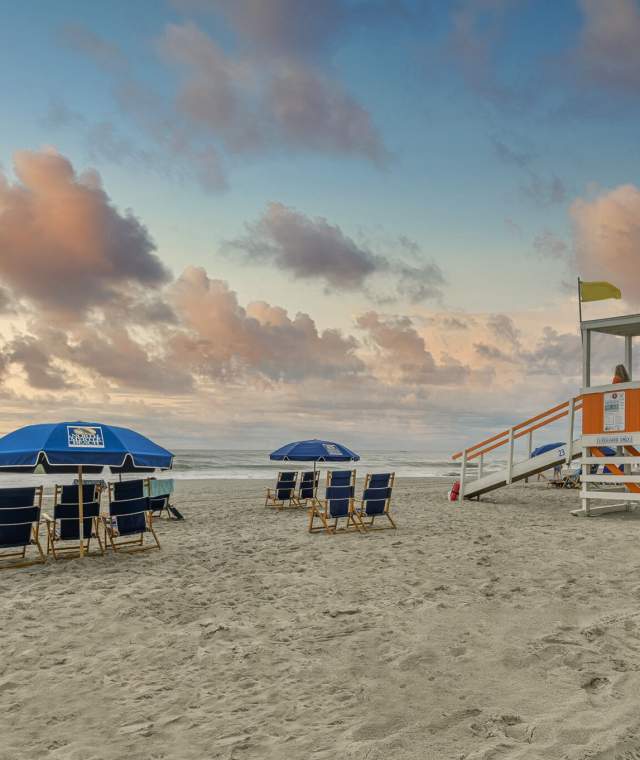 A beautiful sunrise in North Myrtle Beach with beach chairs, umbrellas, and lifeguard stand.