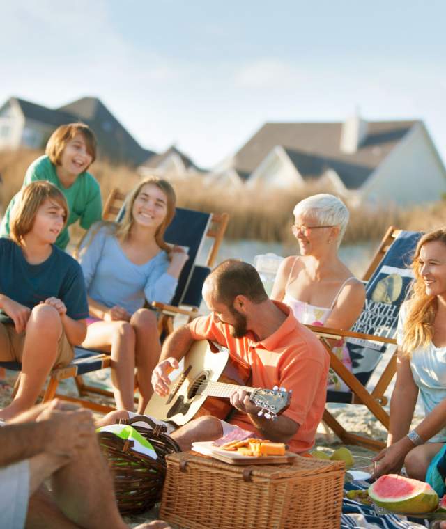 Friends having an oceanfront picnic with beach houses in the background.