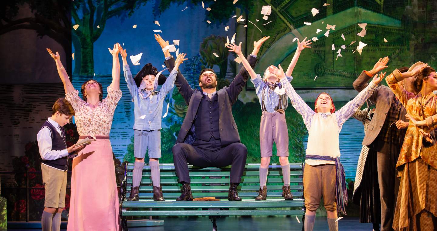theatre stage with cast raising arms into air